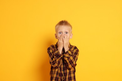 Scared little boy covering mouth on orange background