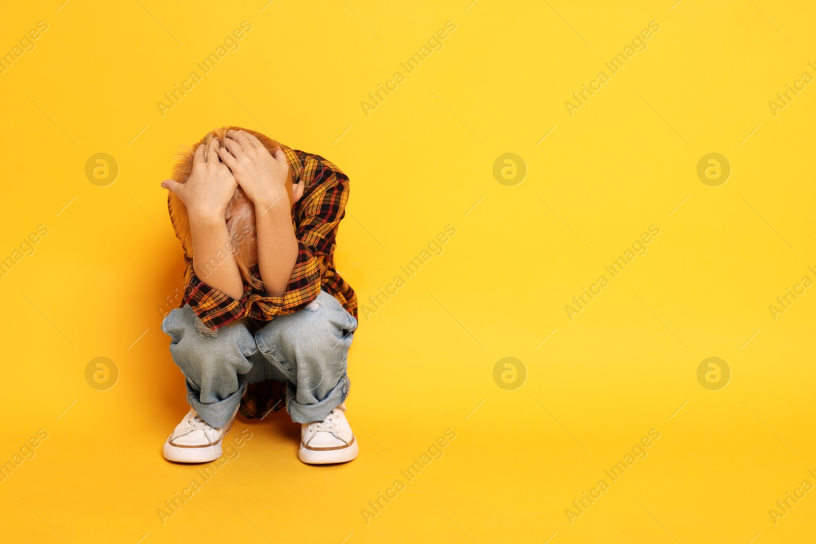 Photo of Scared little boy hiding on orange background. Space for text