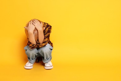 Scared little boy hiding on orange background. Space for text