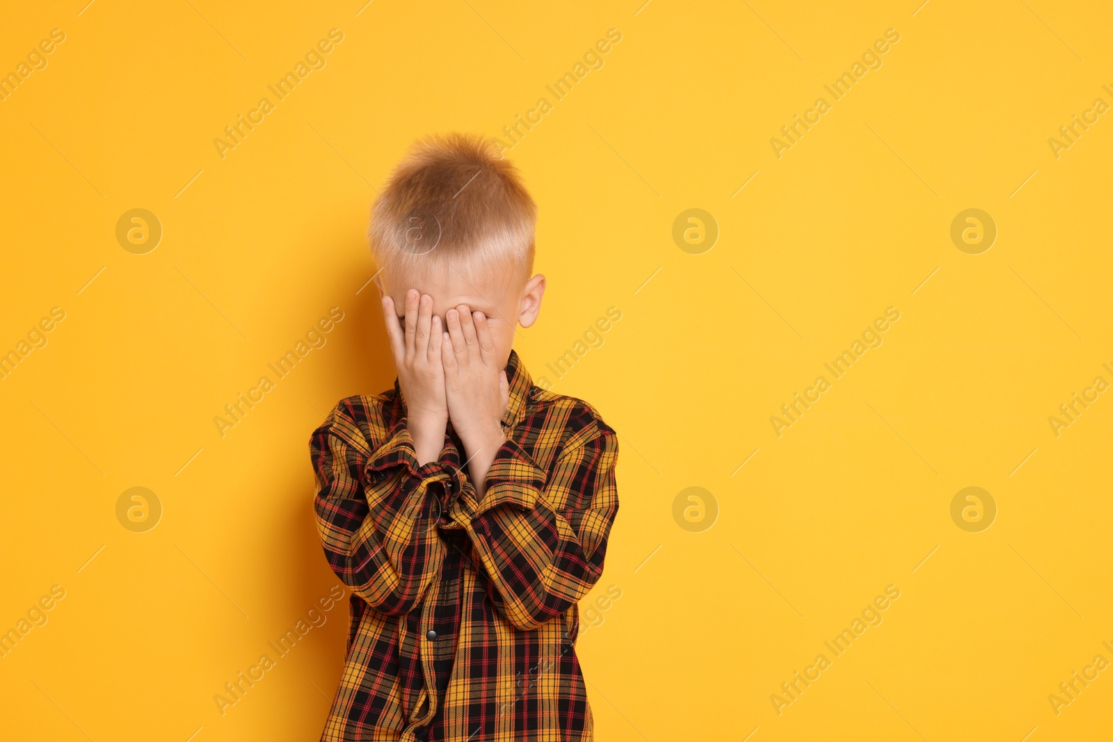 Photo of Scared little boy covering face on orange background. Space for text