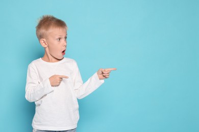 Scared little boy pointing at something on light blue background. Space for text