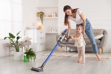 Smiling young woman and her daughter cleaning floor with cordless vacuum cleaner at home