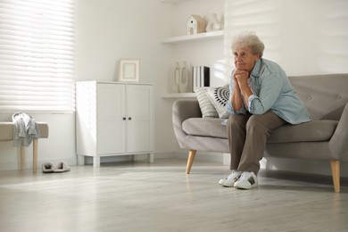 Photo of Loneliness concept. Sad senior woman sitting on sofa at home