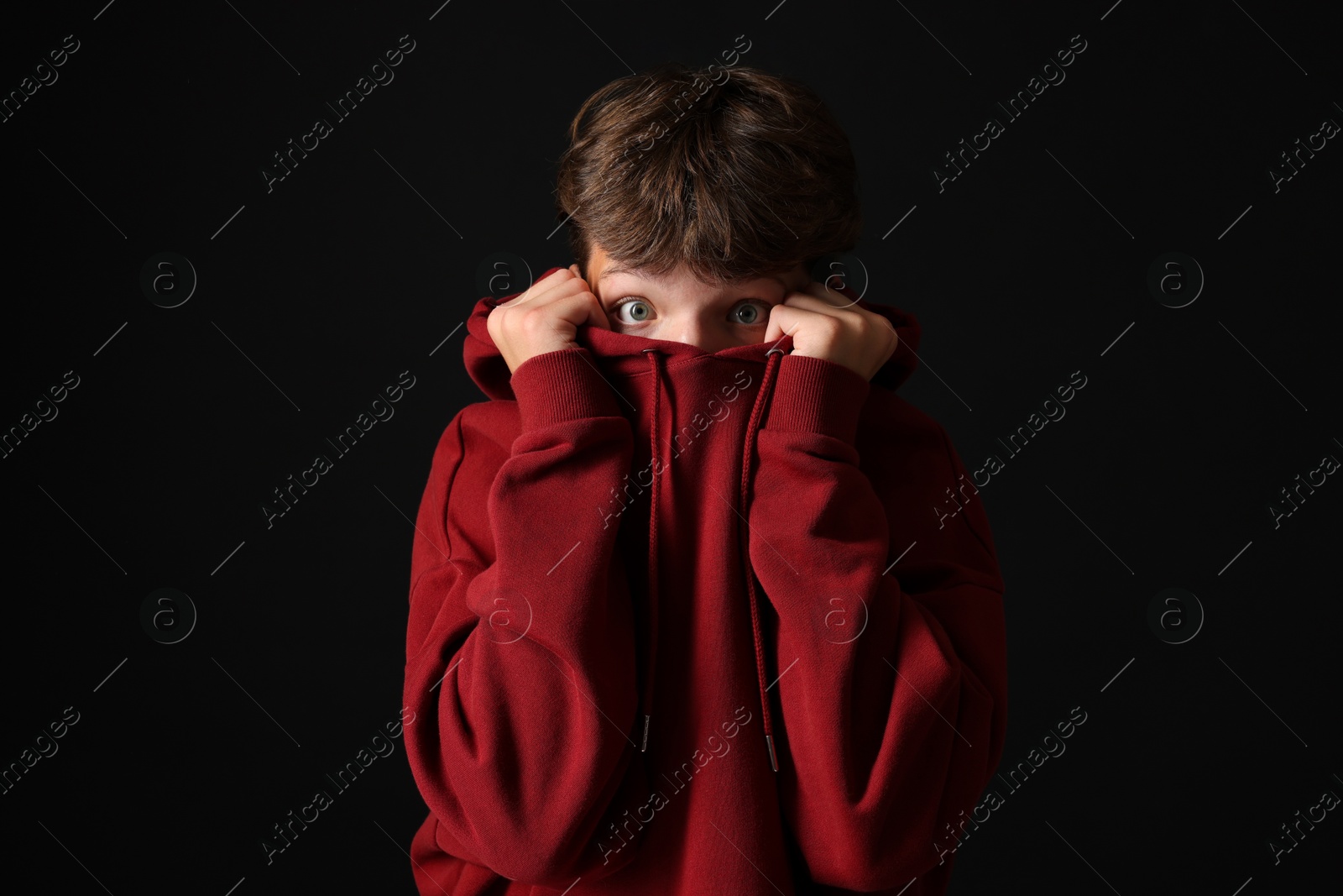 Photo of Scared teenage boy hiding on black background