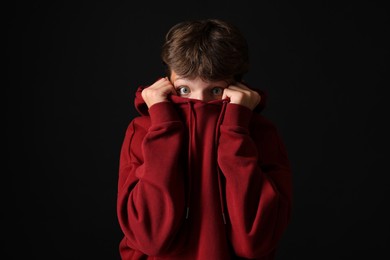 Photo of Scared teenage boy hiding on black background