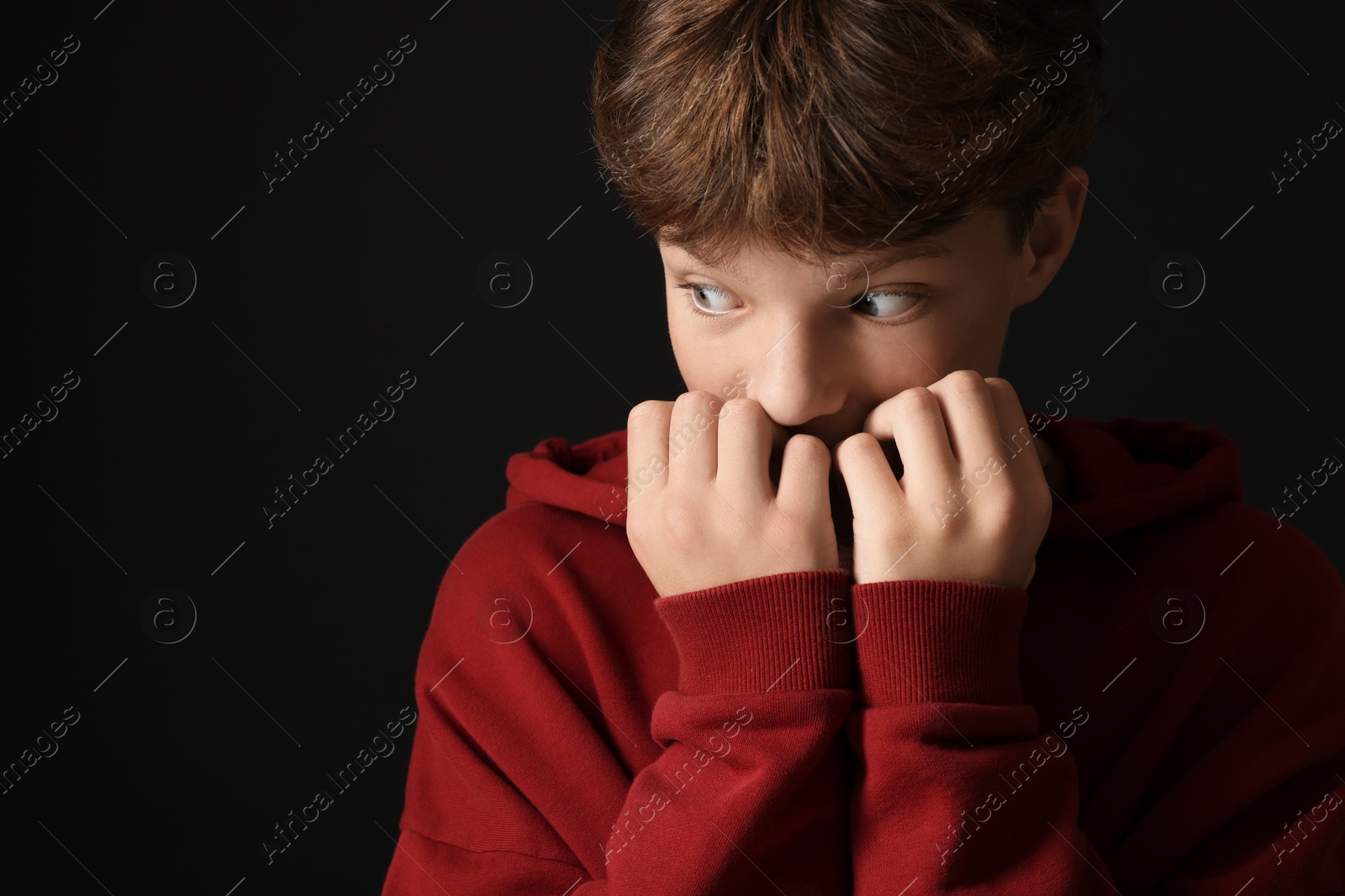 Photo of Scared teenage boy on black background. Space for text