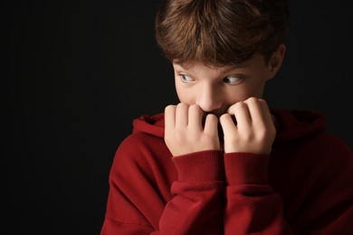 Scared teenage boy on black background. Space for text