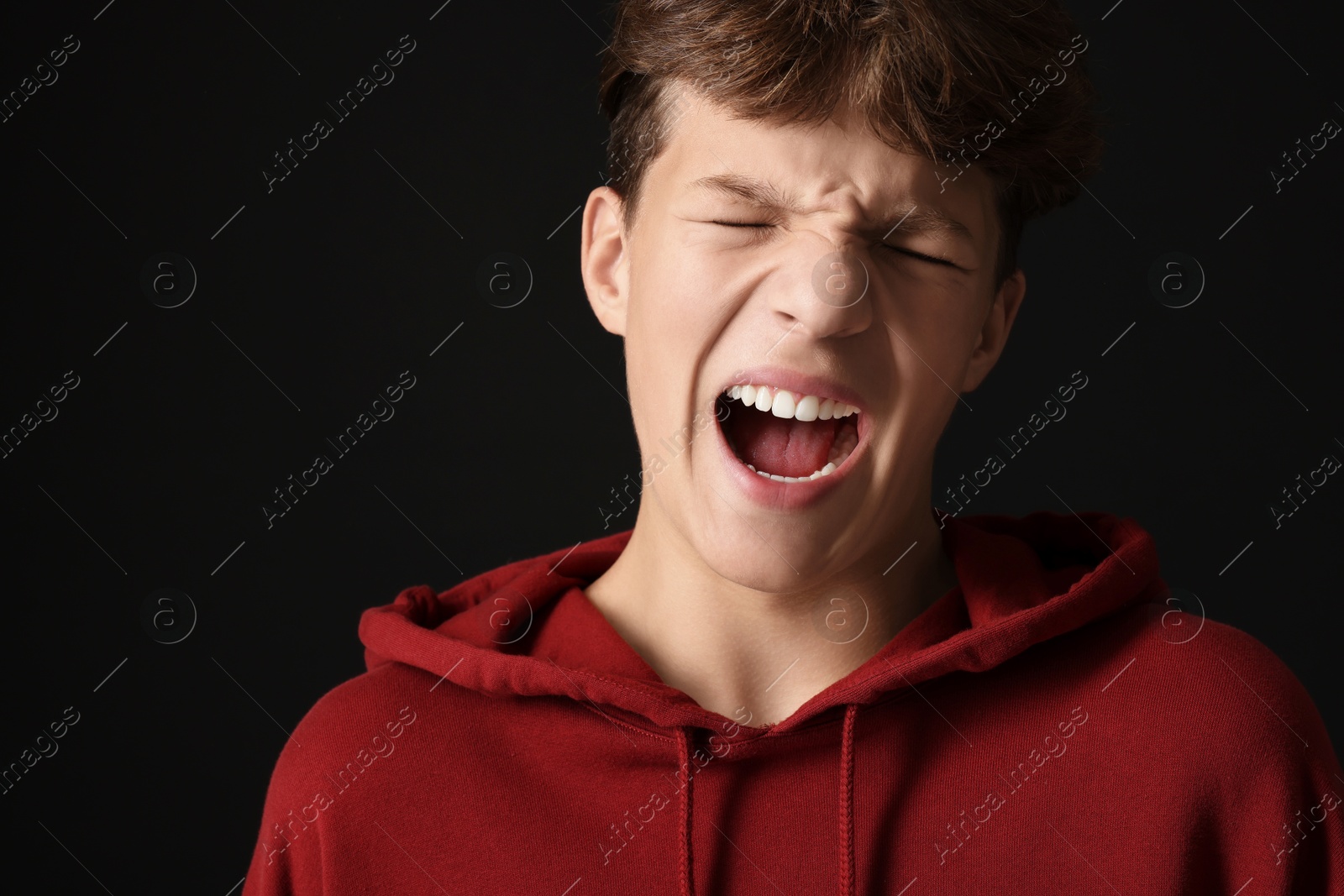 Photo of Scared teenage boy screaming on black background. Space for text