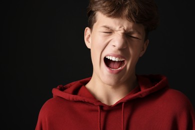 Photo of Scared teenage boy screaming on black background. Space for text