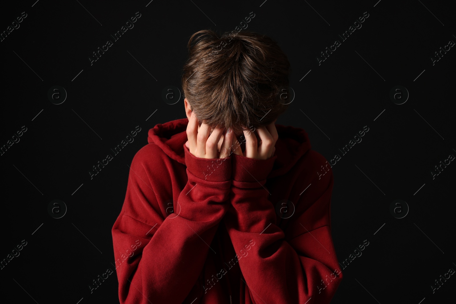 Photo of Scared teenage boy covering face with hands on black background