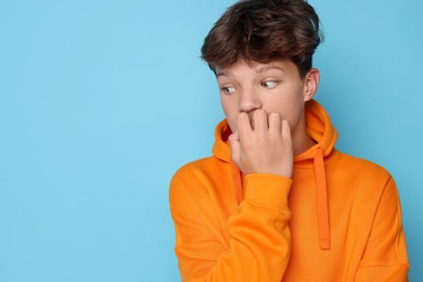 Photo of Scared teenage boy on light blue background. Space for text