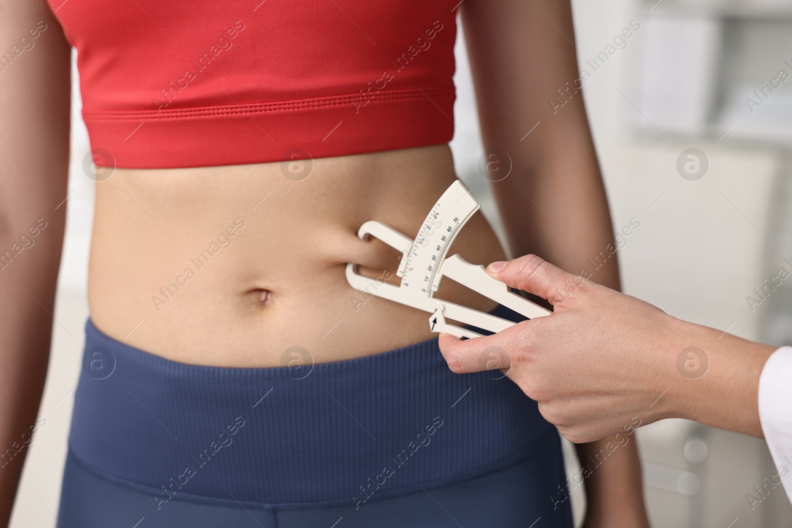 Photo of Doctor measuring woman's body fat with caliper in clinic, closeup