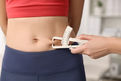 Photo of Doctor measuring woman's body fat with caliper in clinic, closeup