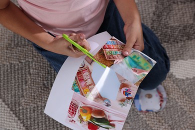 Creating vision board. Girl cutting out picture on floor indoors, top view