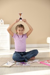 Creating vision board. Girl with picture of golden cup trophy on floor indoors