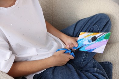 Photo of Creating vision board. Girl cutting out picture in armchair, closeup