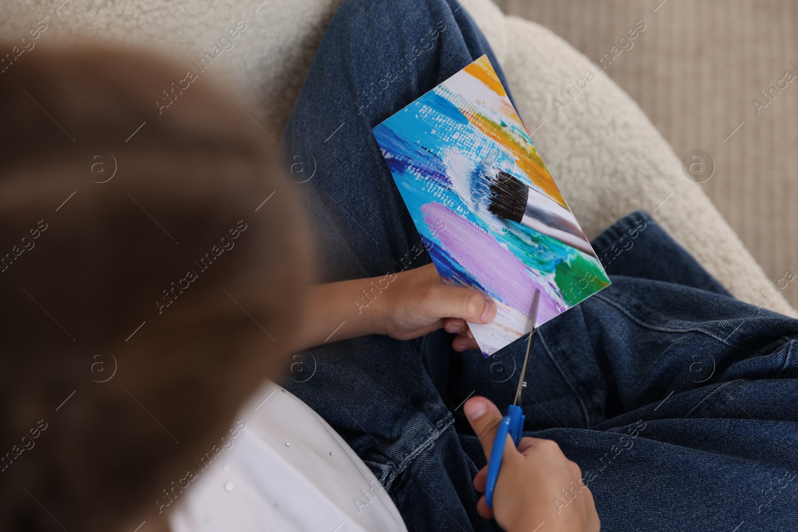 Photo of Creating vision board. Girl cutting out picture in armchair, top view