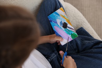 Photo of Creating vision board. Girl cutting out picture in armchair, top view