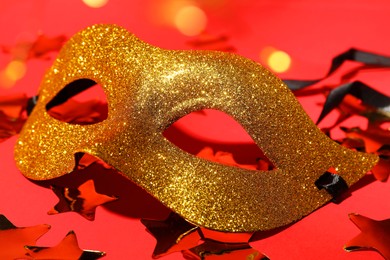 Photo of Beautiful golden carnival mask and confetti on red background, closeup