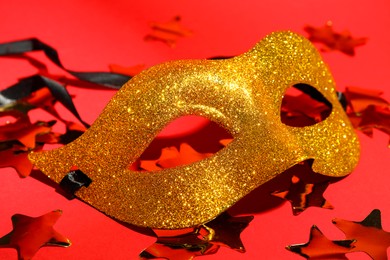 Photo of Beautiful golden carnival mask and confetti on red background, closeup