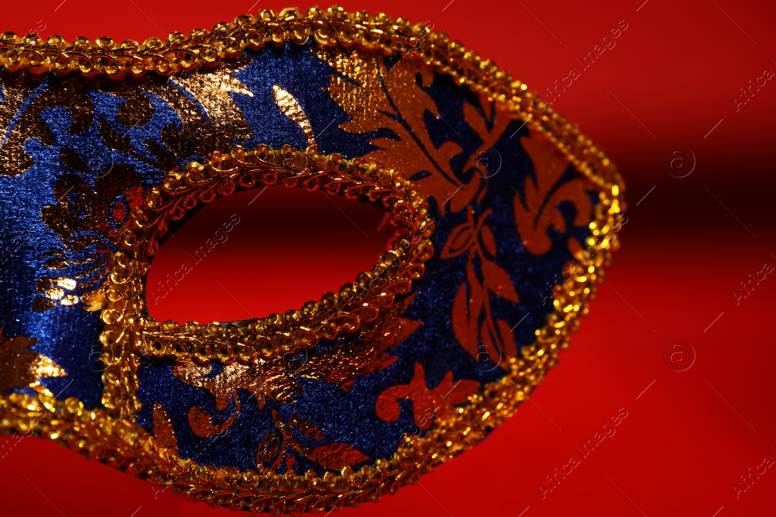 Photo of Beautiful blue carnival mask on red background, closeup