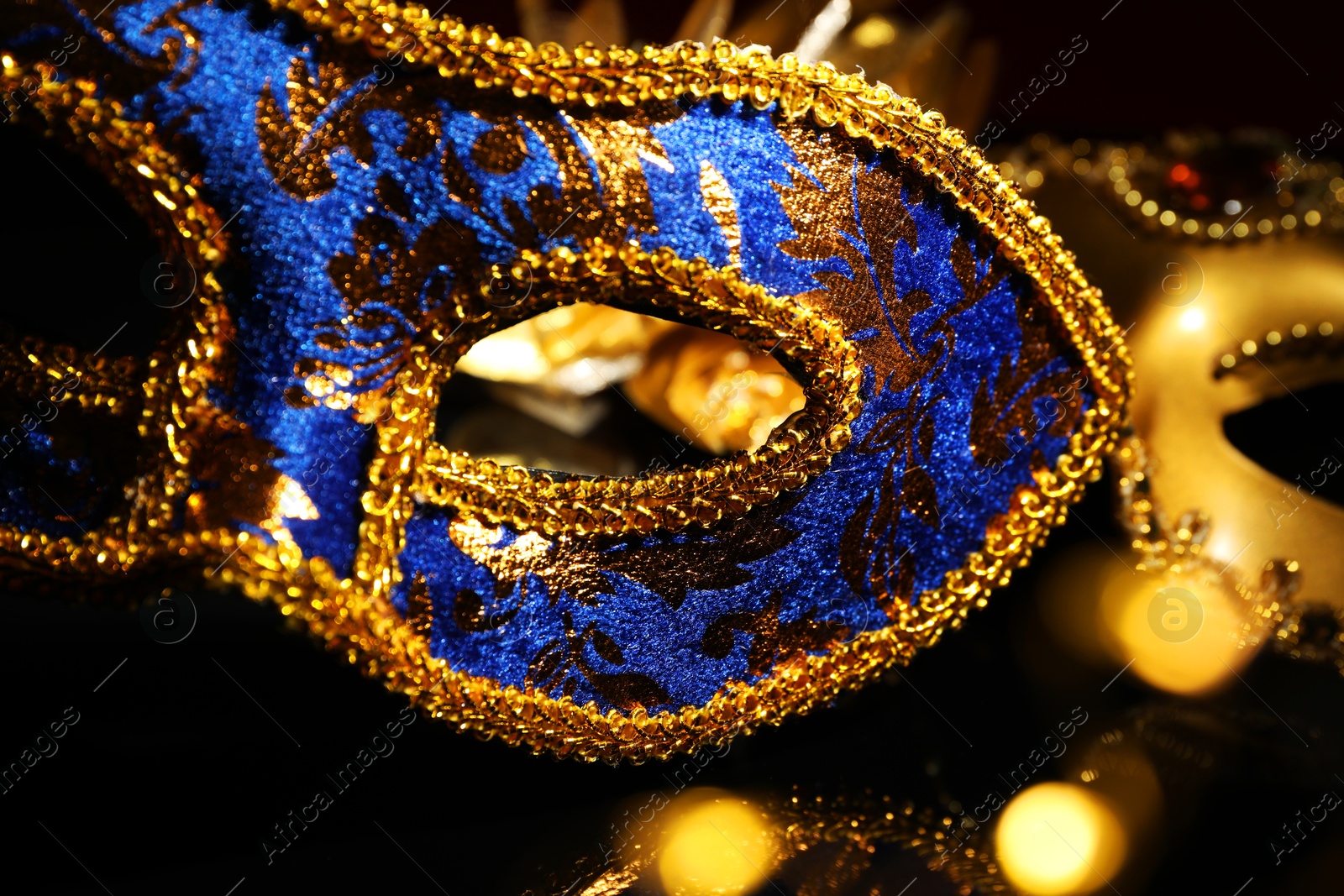 Photo of Beautiful blue carnival mask on black background, closeup. Bokeh effect