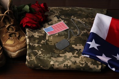 Photo of Veterans day. USA army patch, token, American flag, roses and military uniform on wooden table, closeup