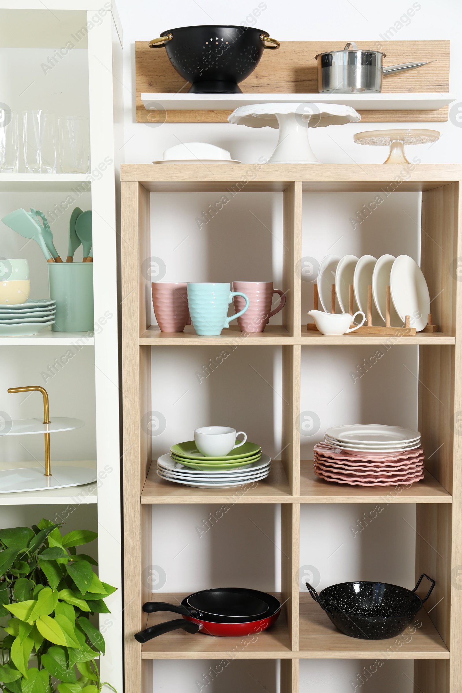 Photo of Shelving units with kitchenware near white wall indoors