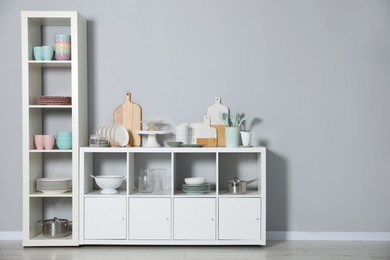 Photo of Shelving unit and storage cabinet with kitchenware near grey wall indoors