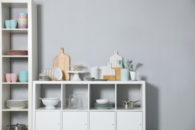 Photo of Shelving unit and storage cabinet with kitchenware near grey wall indoors