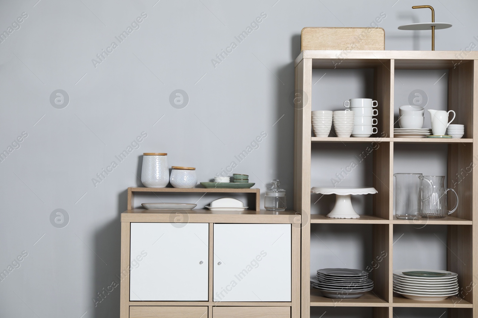 Photo of Wooden shelving unit and storage cabinet with kitchenware near grey wall indoors