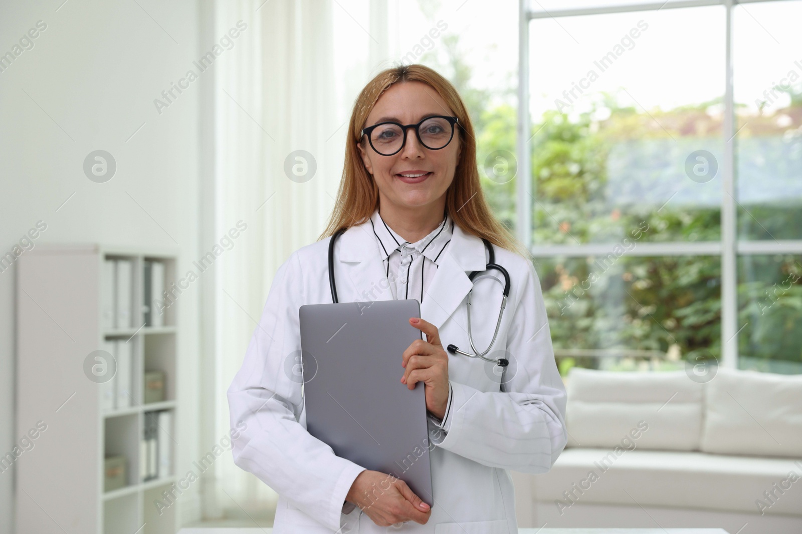 Photo of Smiling doctor with stethoscope and laptop in clinic