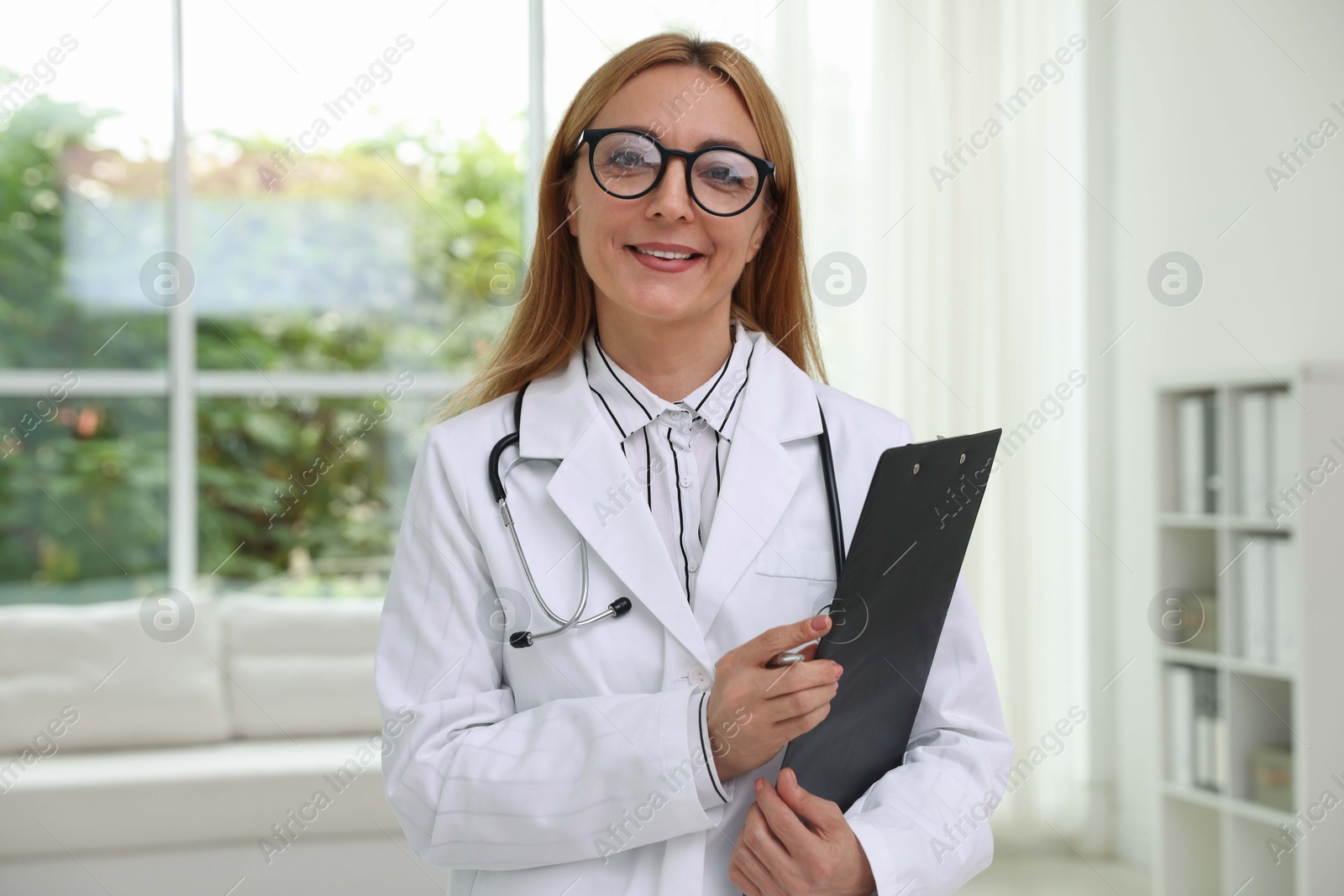 Photo of Smiling doctor with stethoscope and clipboard in clinic