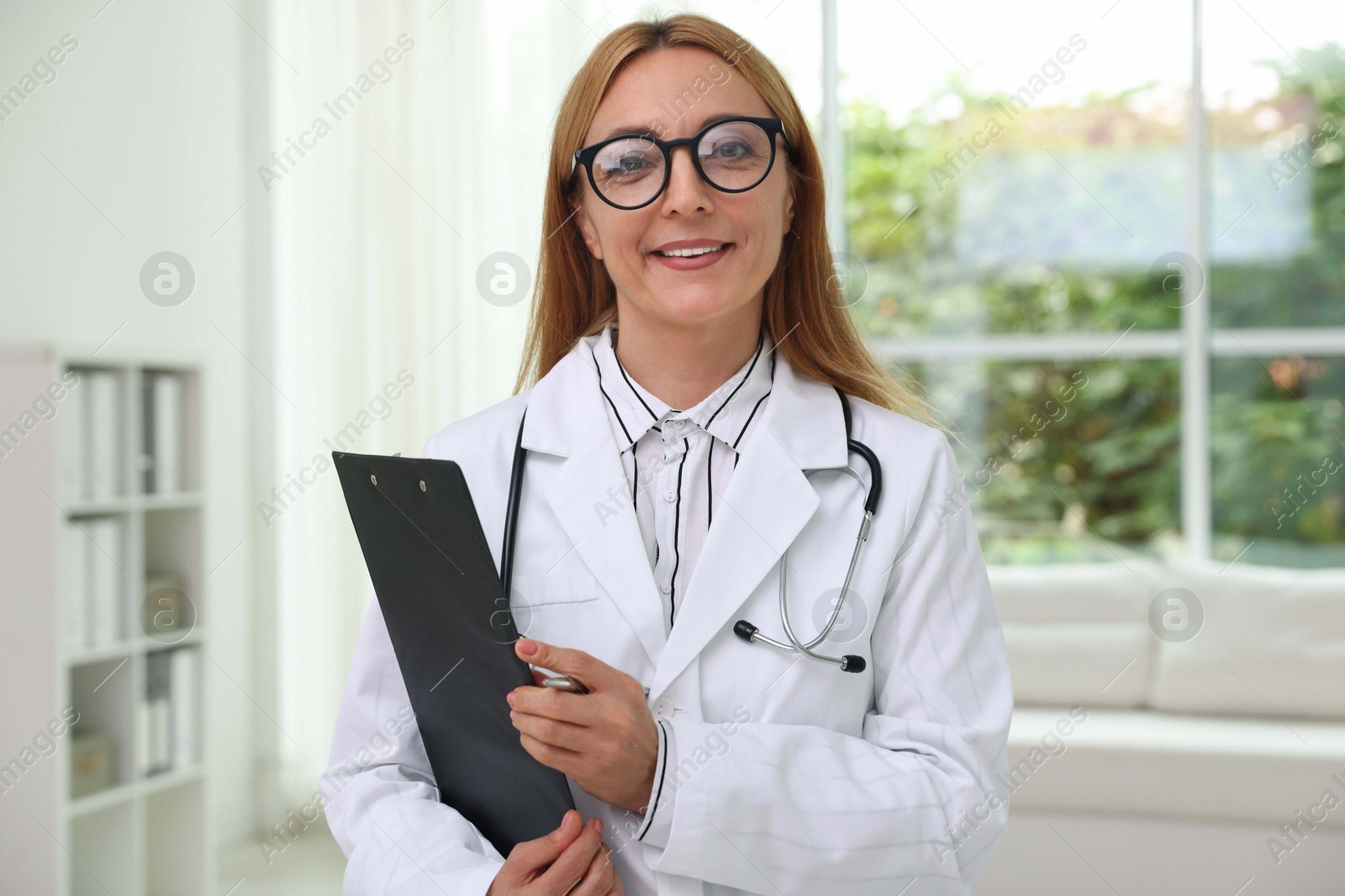 Photo of Smiling doctor with stethoscope and clipboard in clinic