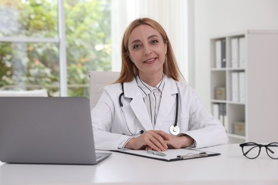 Doctor with stethoscope, laptop and clipboard at table in clinic