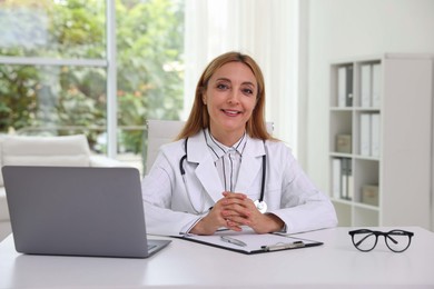 Doctor with stethoscope, laptop and clipboard at table in clinic