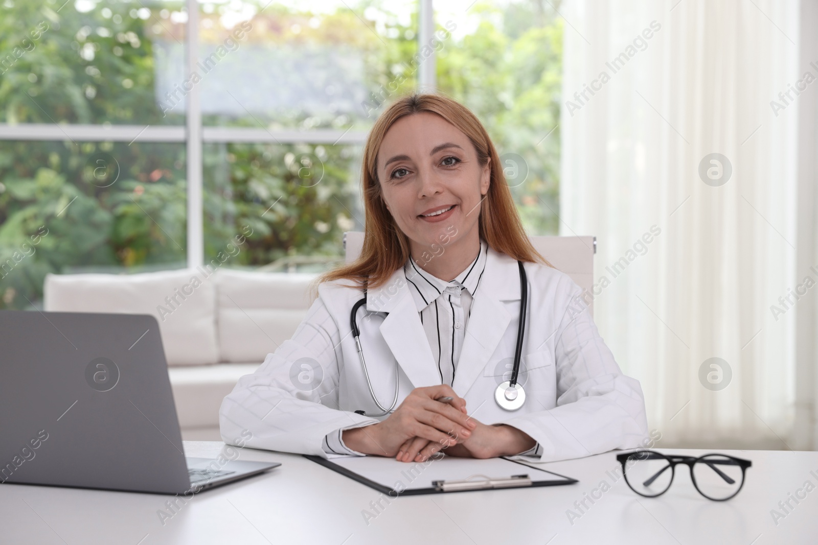 Photo of Doctor with stethoscope, laptop and clipboard at table in clinic