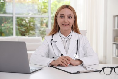 Doctor with stethoscope, laptop and clipboard at table in clinic