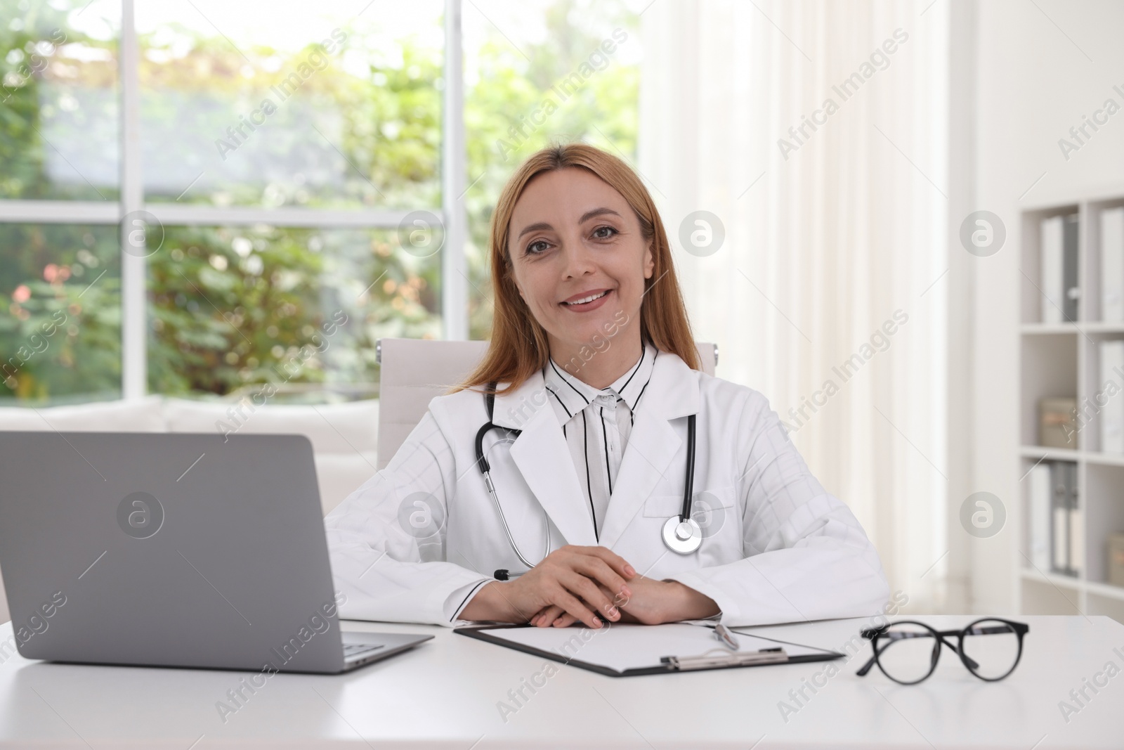 Photo of Doctor with stethoscope, laptop and clipboard at table in clinic