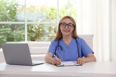 Photo of Doctor with stethoscope, laptop and clipboard at table in clinic