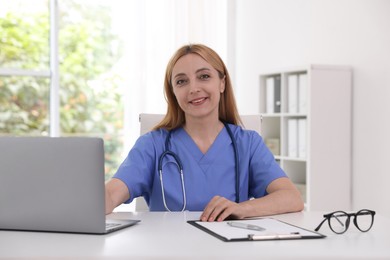 Doctor with stethoscope, laptop and clipboard at table in clinic