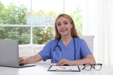 Doctor with stethoscope, laptop and clipboard at table in clinic