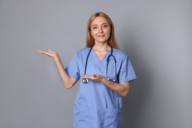 Doctor with stethoscope showing something on gray background