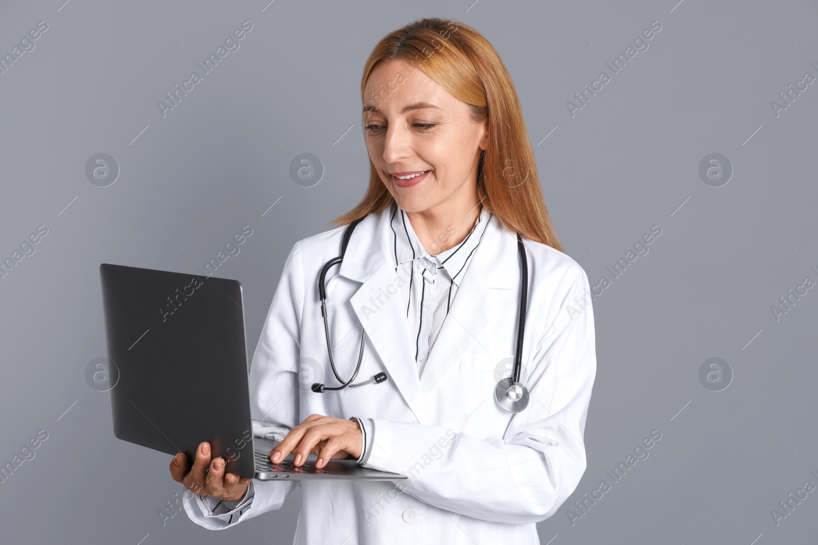 Photo of Doctor with stethoscope and laptop on gray background