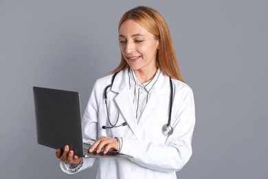 Photo of Doctor with stethoscope and laptop on gray background