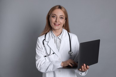 Doctor with stethoscope and laptop on gray background