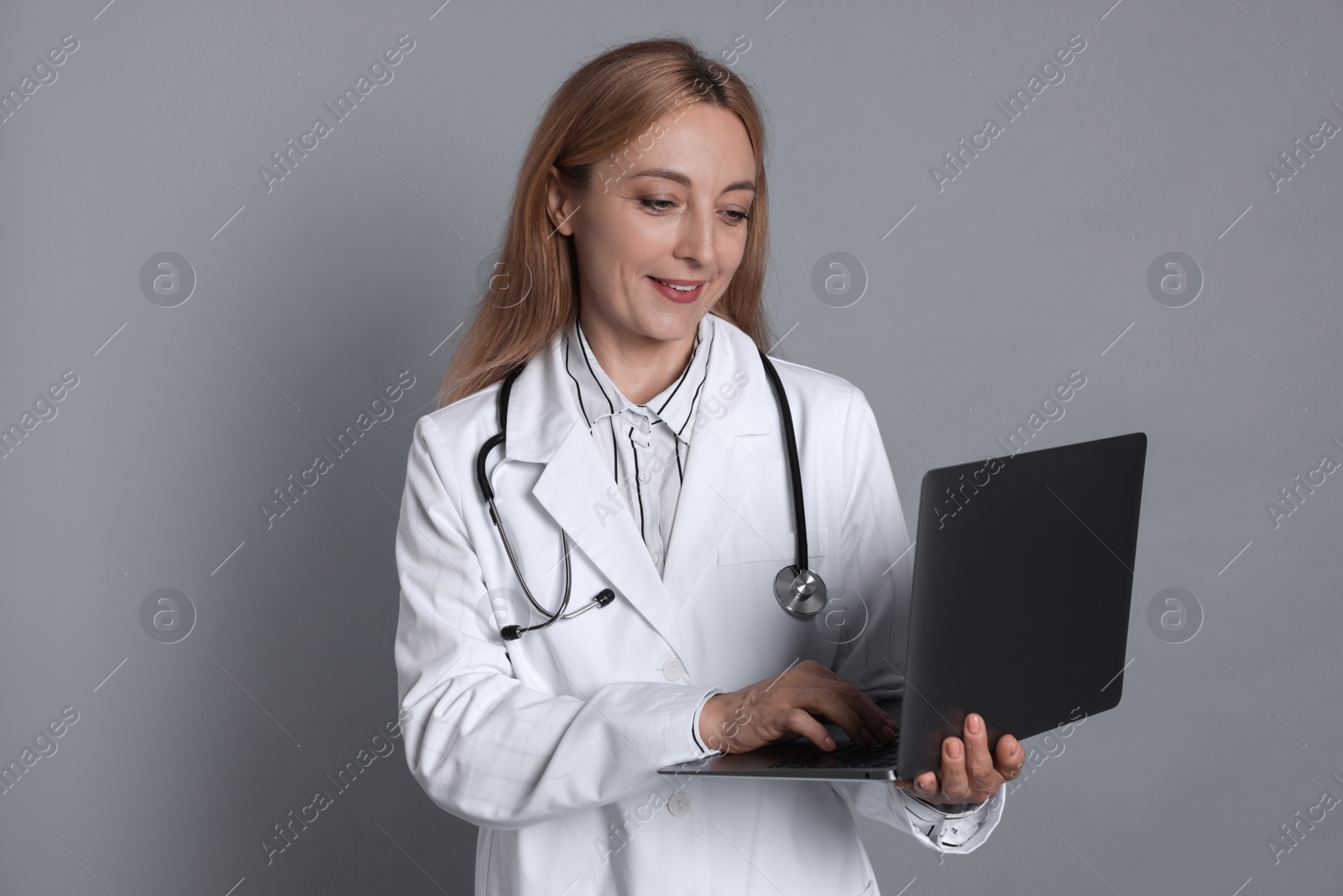 Photo of Doctor with stethoscope using laptop on gray background