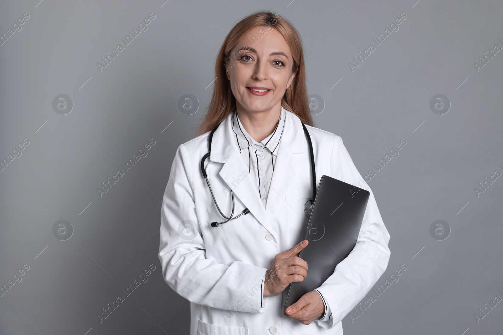 Photo of Doctor with stethoscope and laptop on gray background