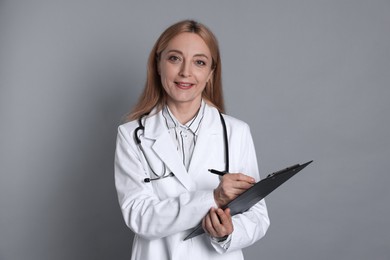 Doctor with clipboard writing notes on gray background