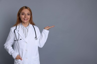 Doctor with stethoscope showing something on gray background, space for text